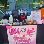 Ice cream sundae bar setup with various toppings and a pink sign advertising ice cream, sundaes, and shakes.